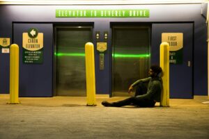 Un homme assis près d'une entrée d'ascenseur sous des néons la nuit.